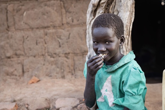 Uganda: young boy looking at the camera with a slight smile while eating