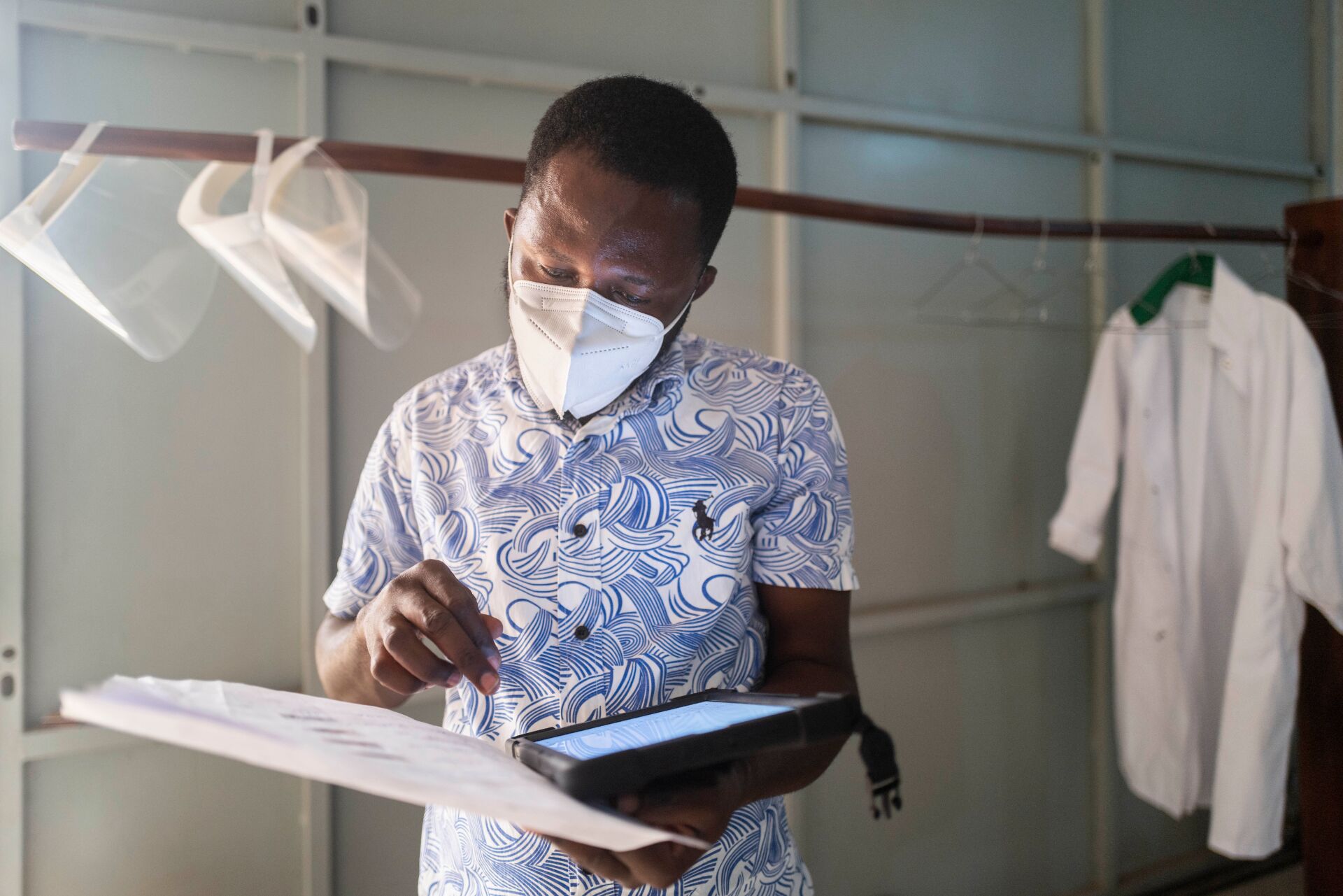 A man, wearing a face mask, reviews a list of data that he is holding in his hands.
