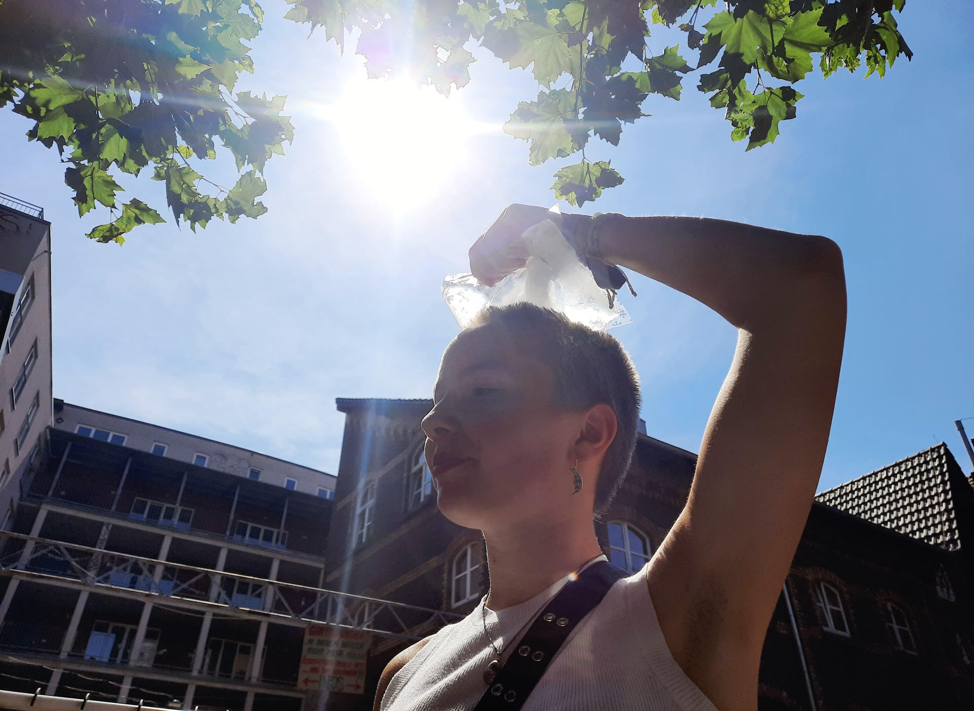 Young lady holding an icepack on her head to cool down during heat in urban environment.