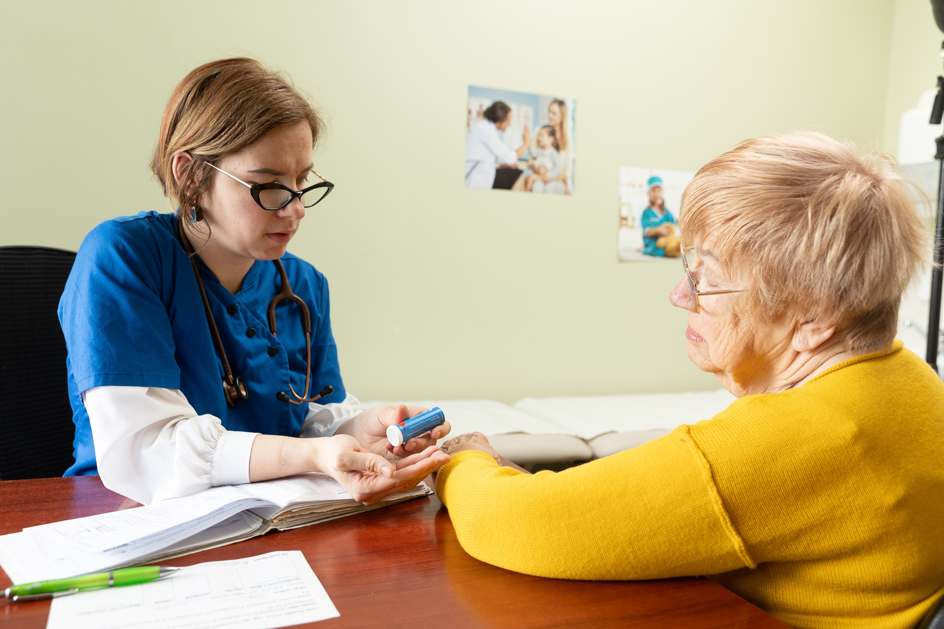 An older woman sits in a medical room in Riga, engaged in conversation with her doctor.